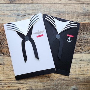 May include: Two white and black paper cards with a sailor's uniform design. One card has a submarine emblem and the other has an anchor emblem.