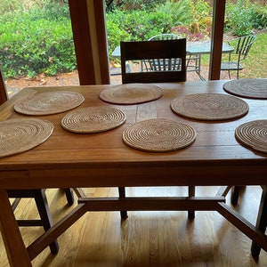 Puede incluir: Una mesa de madera con seis manteles individuales tejidos en forma circular. Los manteles individuales son de color marrón claro y beige. La mesa es de madera y tiene un acabado natural.