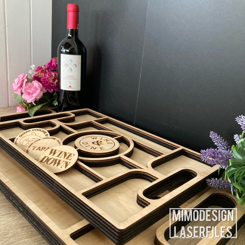 K&ouml;nnte beinhalten: Ein Holztablett mit mehreren F&auml;chern und einem schwarzen Rand. Das Tablett hat ein "Wine & Dine"-Etikett und ein "Tap Wine Down"-Etikett. Das Tablett steht auf einer schwarzen Oberfl&auml;che mit einer Weinflasche und Blumen.