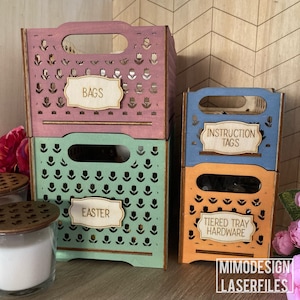 May include: Four wooden storage crates with tulip designs and labels. The crates are stacked on top of each other. The top crate is pink and labeled "Bags". The second crate is green and labeled "Easter". The third crate is blue and labeled "Instruction Tags". The bottom crate is orange and labeled "Tiered Tray Hardware".