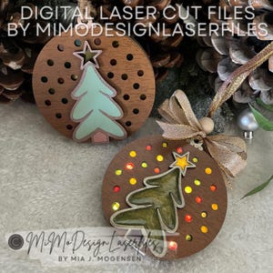 Puede incluir: Dos adornos navideños de madera con un diseño de árbol de Navidad cortado con láser. Los adornos son marrones con una veta de madera marrón claro. El árbol del adorno de la izquierda es azul claro y verde, mientras que el árbol del adorno de la derecha es verde con una estrella amarilla en la parte superior. Los adornos están decorados con pequeños puntos de colores.