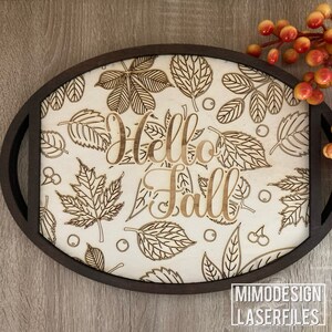 Può includere: Un vassoio di servizio in legno con una cornice marrone e un inserto bianco. L'inserto presenta un motivo di foglie e il testo "Hello Fall".