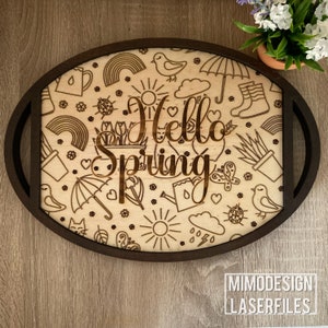 Può includere: Un vassoio di legno con una cornice ovale marrone e un design a taglio laser di illustrazioni a tema primaverile, tra cui fiori, farfalle, arcobaleni e il testo "Hello Spring".