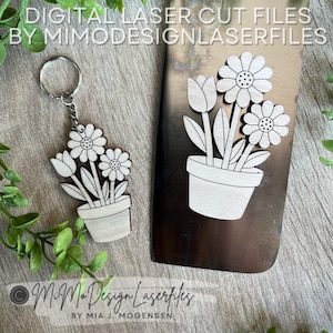 May include: Wooden flower-themed keychain and decorative element. The keychain features a flower pot with daisies and a tulip. The decorative element has a similar design. The text "DIGITAL LASER CUT FILES BY MIMODESIGNLASERFILES" is visible.
