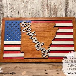 May include: A wooden cutout of the state of Arkansas with the word "Arkansas" in cursive script, superimposed on a wooden American flag. The flag is painted in red, white, and blue. The text "MiMoDesignLaserfiles DIGITAL FILES ONLY! SVG+DXF FOR LASER CUTTING Instant Download" is visible in the lower right corner.