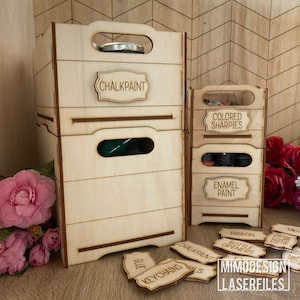 May include: Wooden storage boxes with labels for organising craft supplies. The labels include "Chalkpaint", "Colored Sharpies", "Enamel Paint", "Ribbon", "Bottle Openers", "Glue", "Keychains", "Tags", and "Chalkpaint".