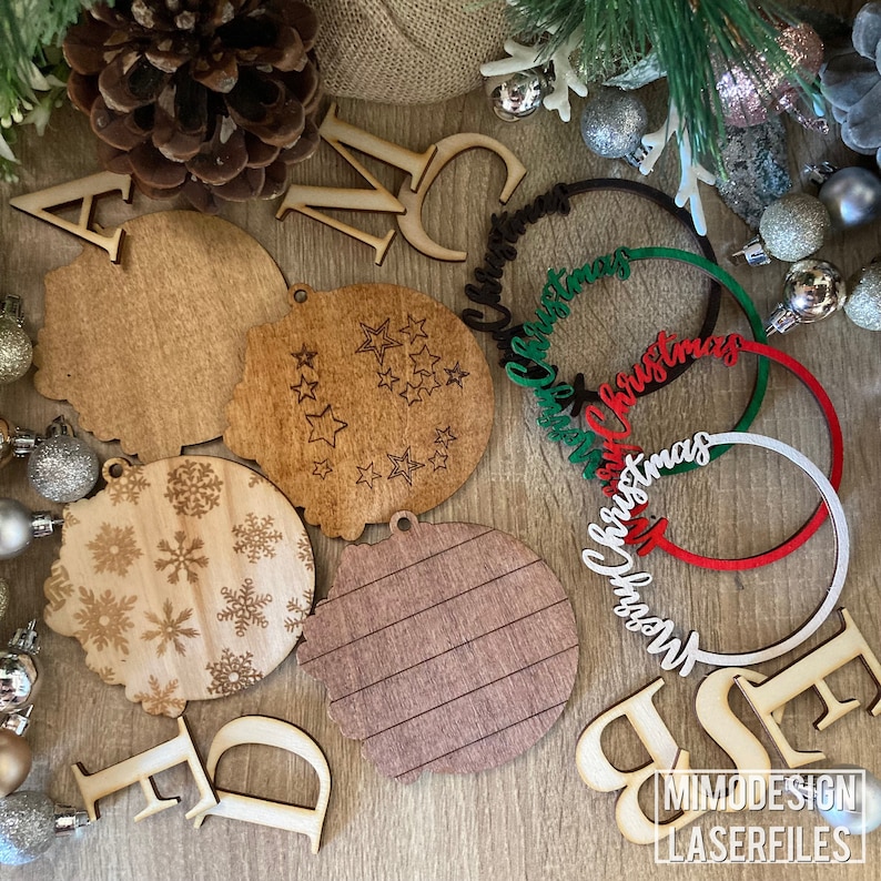 Op de afbeelding: Een set lasergesneden houten kerstversieringen, waaronder een ronde kerstbal met een sneeuwvlokkenpatroon, een ronde kerstbal met een sterrenpatroon, een ronde kerstbal met een gestreept patroon en een ronde kerstbal met de tekst "Merry Christmas".
