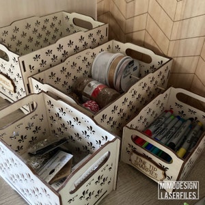 May include: Four wooden storage boxes with a decorative floral pattern. The boxes are stacked on top of each other and contain various craft supplies, including ribbon, twine, and markers. The top box has a label that says "Fine Tip Sharpies".
