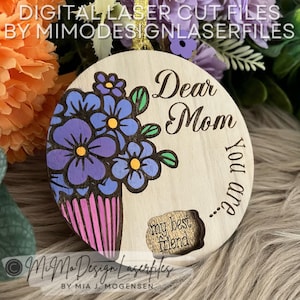 Può includere: Un ornamento rotondo in legno con un design tagliato al laser. Il design presenta un bouquet di fiori viola con centri gialli e uno stelo a strisce rosa e bianche. Il testo "Dear Mom You are my best friend..." è inciso sull'ornamento.