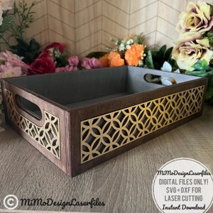 Può includere: Un vassoio di legno con un motivo geometrico decorativo tagliato sui lati. Il vassoio è marrone con un motivo dorato. Il vassoio è appoggiato su una superficie di legno.