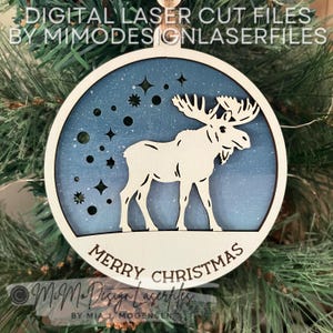 May include: A round wooden ornament with a blue and white starry sky design. A white moose stands in the center of the ornament. The text "Merry Christmas" is written in brown lettering at the bottom of the ornament.