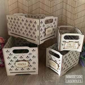 May include: Four wooden storage boxes with cut-out designs and labels. The boxes are stacked on top of each other. The labels read "Ribbon", "Fine Tip Sharpies", "Earrings Hardware", and "Pencils".