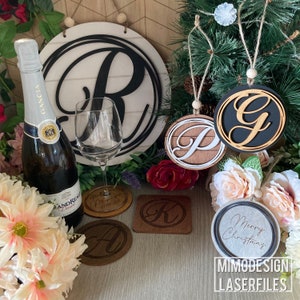 Può includere: Un set di ornamenti e sottobicchieri in legno tagliati al laser che presentano varie lettere e la frase "Buon Natale". Gli ornamenti sono appesi a un albero di Natale e i sottobicchieri sono su una superficie di legno.