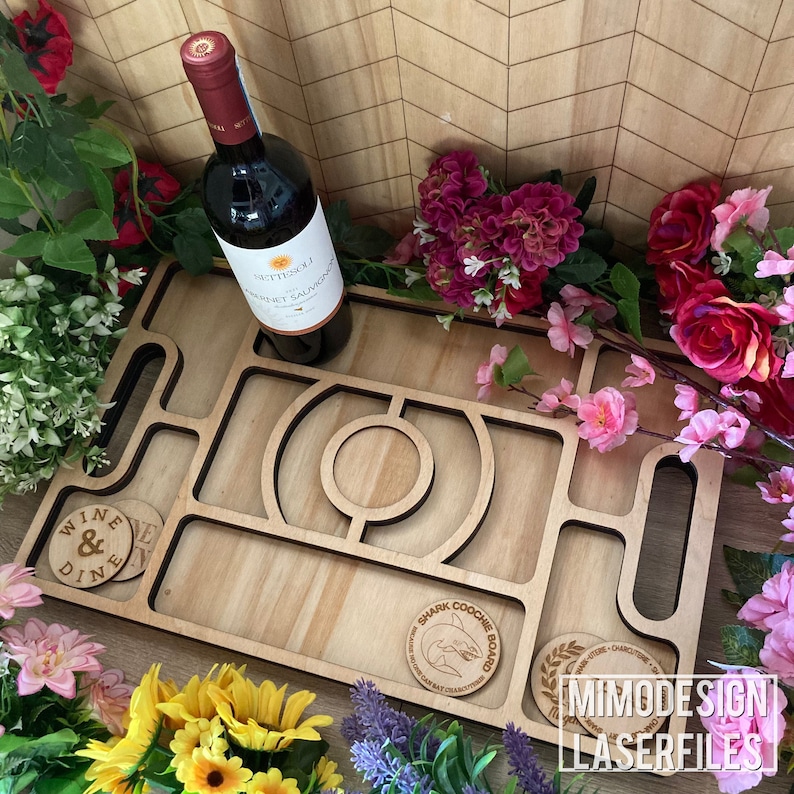 Op de afbeelding: Een houten serveerblad met een haai-ontwerp en de tekst "Shark Coochie Board". Het dienblad heeft meerdere compartimenten en is perfect om snacks en drankjes te serveren. Het dienblad is omringd door bloemen.