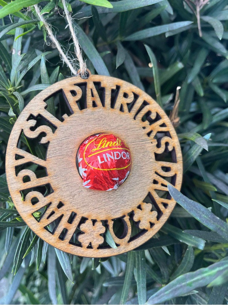 May include: A wooden ornament with the words "Happy St. Patrick's Day" cut out around the edge. A Lindor chocolate is in the center of the ornament.