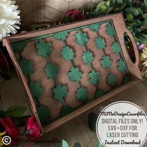 May include: A wooden serving tray with a green shamrock pattern cut out. The tray has a brown wood finish and a handle on the side. The text "MiMoDesignLaserfiles DIGITAL FILES ONLY! SVG+DXF FOR LASER CUTTING Instant Download" is printed on the bottom right corner of the tray.