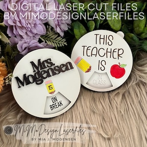 Op de afbeelding: Twee ronde houten borden met een draaibaar wijzerplaat. Het bovenste bord zegt "This Teacher Is" met een potlood en een appel. Het onderste bord zegt "Mrs. Mogensen Is" met een potlood. De wijzerplaat op het bovenste bord zegt "In de klas" en de wijzerplaat op het onderste bord zegt "Pauze".