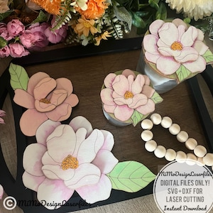 Può includere: Quattro sottobicchieri a forma di fiore di magnolia rosa e bianco con foglie verdi. I sottobicchieri sono su un vassoio di legno con bordo nero. Il testo "Mimo Design Laserfiles" è visibile nell'angolo in basso a destra dell'immagine. SOLO FILE DIGITALI! SVG+DXF PER TAGLIO LASER Download immediato