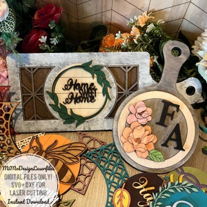 May include: A set of laser cut wooden home decor items, including a sign that says "Home Sweet Home" in a wreath, a round cutting board with a floral design and the initials "FA", and a bee design.