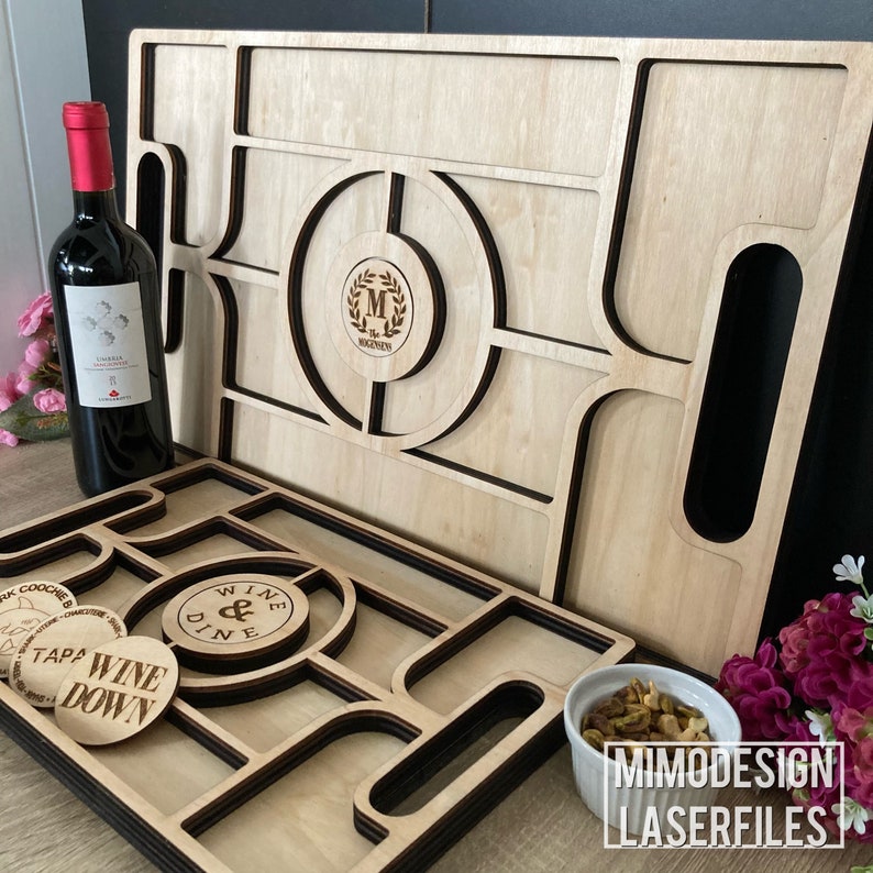 K&ouml;nnte beinhalten: Ein Holztablett mit mehreren F&auml;chern und einem Griff. Das Tablett ist aus hellem Holz mit schwarzen Akzenten. Das Tablett hat einen runden Ausschnitt mit dem Text "Wine & Dine" und einem Monogramm "M" mit einem Lorbeerkranz. Das Tablett ist perfekt zum Servieren von Snacks, Getr&auml;nken und Vorspeisen.