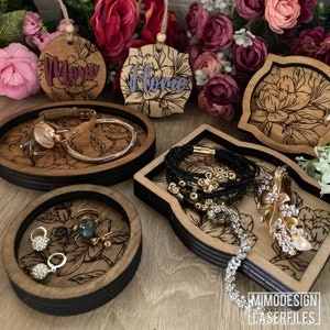 May include: Four wooden trays with floral designs and black trim. The trays are decorated with laser-cut floral patterns and are perfect for organizing jewelry, keys, or other small items. The trays are made of wood and have a natural finish.
