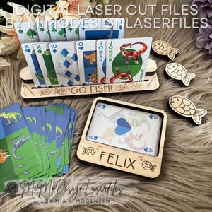 May include: Wooden card holder set with a deck of cards featuring dinosaur illustrations. The set includes a card holder with the text "GO FISH!" and a box with the name "FELIX". Additional wooden fish-shaped cutouts are also present.