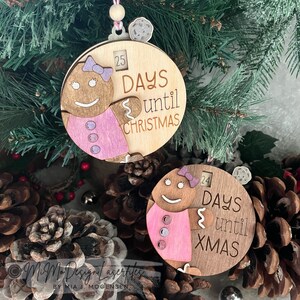 Può includere: Due ornamenti di Natale in legno a forma di pan di zenzero per il conto alla rovescia. Gli ornamenti sono decorati con vernice rosa e marrone e hanno il testo "25 giorni fino a Natale" e "24 giorni fino a Natale".