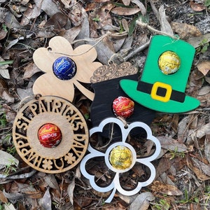 May include: Five wooden ornaments with a shamrock, pot of gold, leprechaun hat, and two other shamrocks. Each ornament has a small chocolate candy in the center.