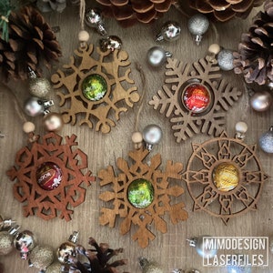 Może przedstawiać: Pięć drewnianych ozdób w kształcie płatka śniegu z czekoladową słodyczą w środku każdej z nich. Płatki śniegu są brązowe i mają wycięty wzór. Czekoladki są owinięte w złotą, czerwoną i zieloną folię.