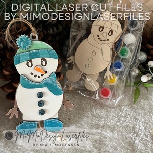 May include: Two unfinished wooden snowman ornaments, one with a blue and green hat and scarf, the other with a brown hat and scarf. Both snowmen have a carrot nose and black button eyes. The snowmen are in a clear plastic bag with small bottles of paint.