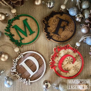 Op de afbeelding: Vier houten kerstversieringen met verschillende letters en ontwerpen. De versieringen zijn rond en hebben een rustieke houtnerfstructuur. De letters zijn M, F, D en C. De ontwerpen omvatten sneeuwvlokken, sterren en een houtnerfpatroon.