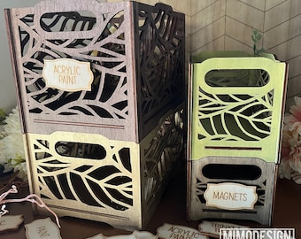 Puede incluir: Dos cajas de almacenamiento de madera con un diseño de hojas. La caja superior es marrón y dice "Pintura acrílica" en una etiqueta. La caja inferior es verde y dice "Imanes" en una etiqueta. Hay varias etiquetas de madera con palabras como "Pintura", "Pegatinas" y "Pintura acrílica" esparcidas alrededor de las cajas.