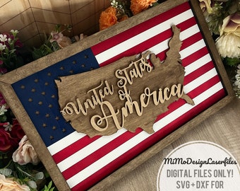 May include: A wooden sign with a red, white, and blue American flag design. The sign features a cutout of the United States with the words "United States of America" written in a cursive font.