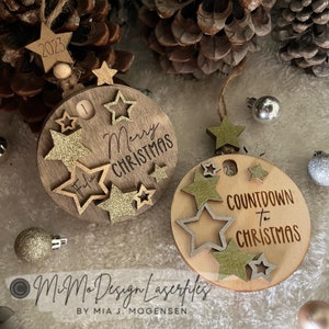 Può includere: Due ornamenti natalizi in legno con un tema di conto alla rovescia fino a Natale. Il primo ornamento è marrone con stelle dorate glitterate e il testo "Buon Natale". Il secondo ornamento è marrone chiaro con stelle dorate glitterate e il testo "Conto alla rovescia fino a Natale".