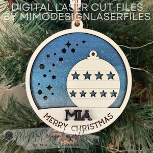 May include: A blue and white wooden Christmas ornament with a star design and the name "MIA" on it. The ornament says "Merry Christmas".