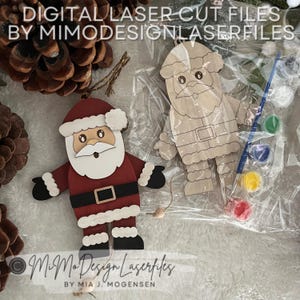 Può includere: Un burattino di Babbo Natale in legno con un vestito rosso, una barba bianca e stivali neri. Il burattino è in una busta di plastica trasparente con vernice e un pennello. Il testo "MiMo Design Laserfiles" è in basso nell'immagine.