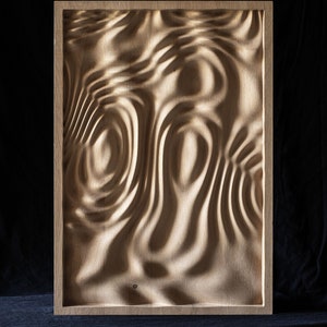 K&ouml;nnte beinhalten: Ein gerahmtes Wandbild aus Holz mit einem geschnitzten Design, das an Wasserwellen erinnert. Das Holz ist hellbraun und der Rahmen ist dunkelbraun.