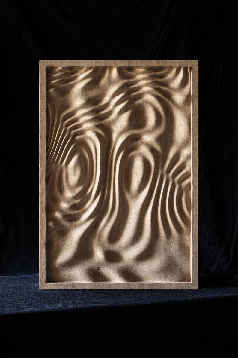 K&ouml;nnte beinhalten: Ein gerahmtes Wandbild aus Holz mit einem geschnitzten Design, das an Wasserwellen erinnert. Das Holz ist hellbraun und der Rahmen ist dunkelbraun.