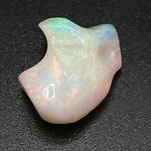 May include: A white opal gemstone with iridescent rainbow colours. The opal is carved into a unique shape, resembling a small animal or a whimsical figure.