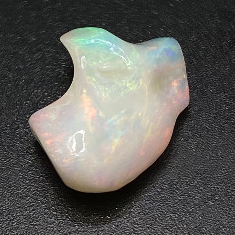 May include: A white opal gemstone with iridescent rainbow colours. The opal is carved into a unique shape, resembling a small animal or a whimsical figure.