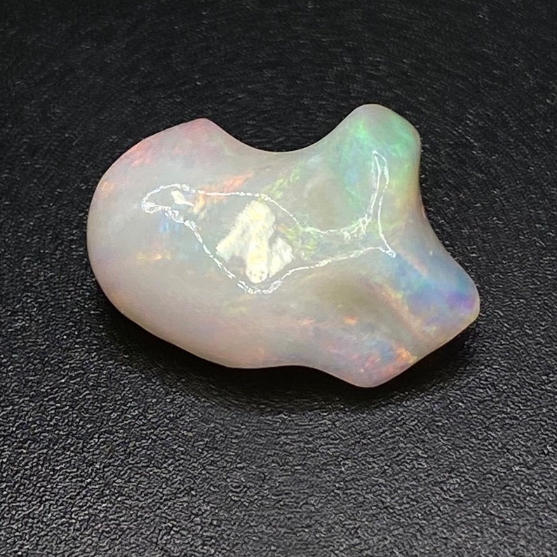 May include: A white opal gemstone with a delicate, hand-drawn design of a bird in white. The opal has a slight iridescent sheen.