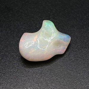 May include: A white opal gemstone with iridescent rainbow colours. The opal has an irregular, organic shape.