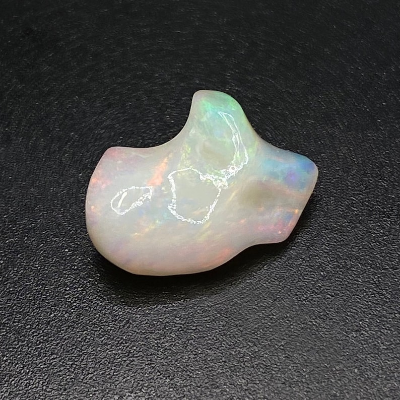 May include: A white opal gemstone with iridescent rainbow colours. The opal has an irregular, organic shape.