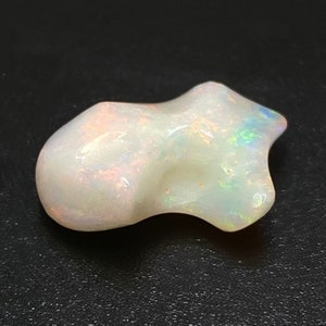 May include: A white opal gemstone with a unique, irregular shape. The opal has a milky white base with flashes of iridescent colour.