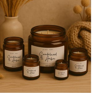 Op de afbeelding: Een verzameling bruine glazen potkaarsen met witte etiketten. De etiketten lezen "Sandalwood & Amber" en bevatten het volume in ml. De kaarsen vari&euml;ren in grootte, de grootste bevat 500 ml.