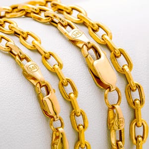 Puede incluir: Una cadena de oro con eslabones ovalados y un cierre de mosquet&oacute;n. Los componentes met&aacute;licos est&aacute;n marcados con el n&uacute;mero 585, que indica la pureza del oro. La cadena tiene un acabado pulido y reflectante con un dise&ntilde;o de eslabones uniforme.