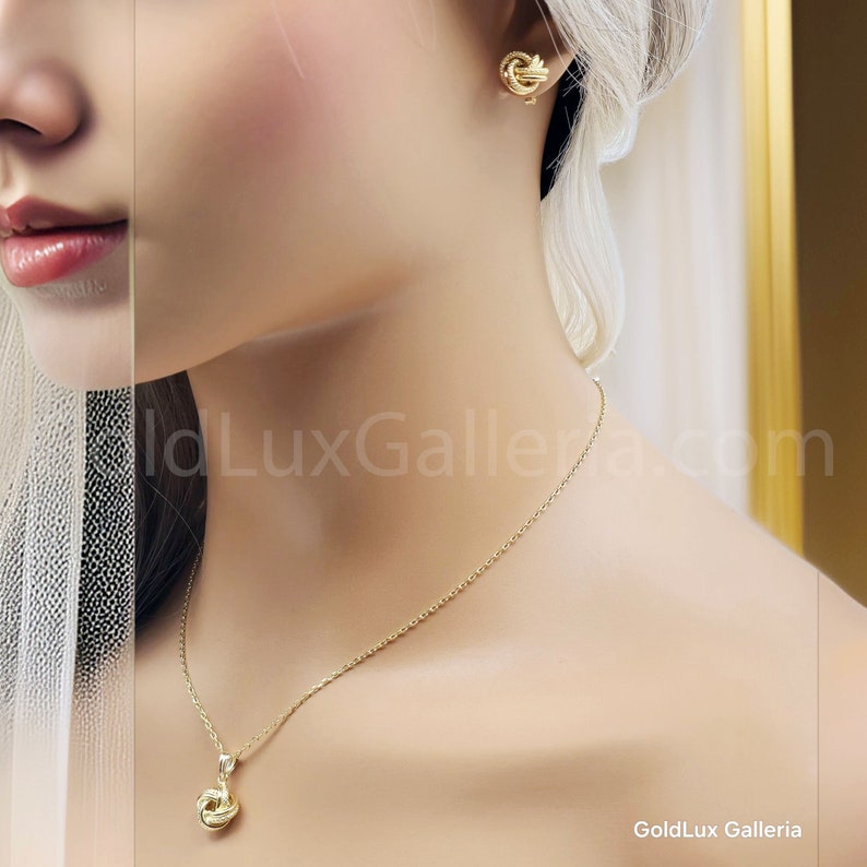 May include: A gold-colored jewelry set featuring a necklace and matching earrings. The necklace has a delicate chain with a knot-shaped pendant. The earrings are also knot-shaped. The jewelry is displayed on a mannequin.