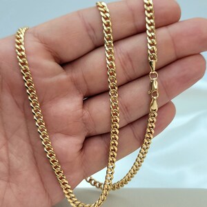 May include: A gold-colored curb chain necklace. The chain is made of interlocking links and has a lobster clasp closure. The necklace is displayed against a light background.