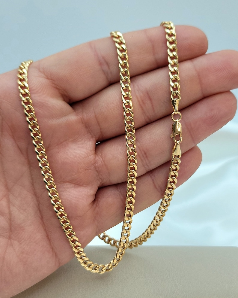 May include: A gold-colored curb chain necklace. The chain is made of interlocking links and has a lobster clasp closure. The necklace is displayed against a light background.