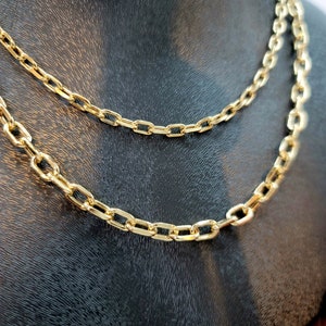 Puede incluir: Un collar de cadena en tono dorado con eslabones rectangulares alargados. La cadena est&aacute; dispuesta en capas, mostrando dos hilos distintos con el mismo dise&ntilde;o de eslabones de metal pulido, creando un aspecto uniforme y brillante.